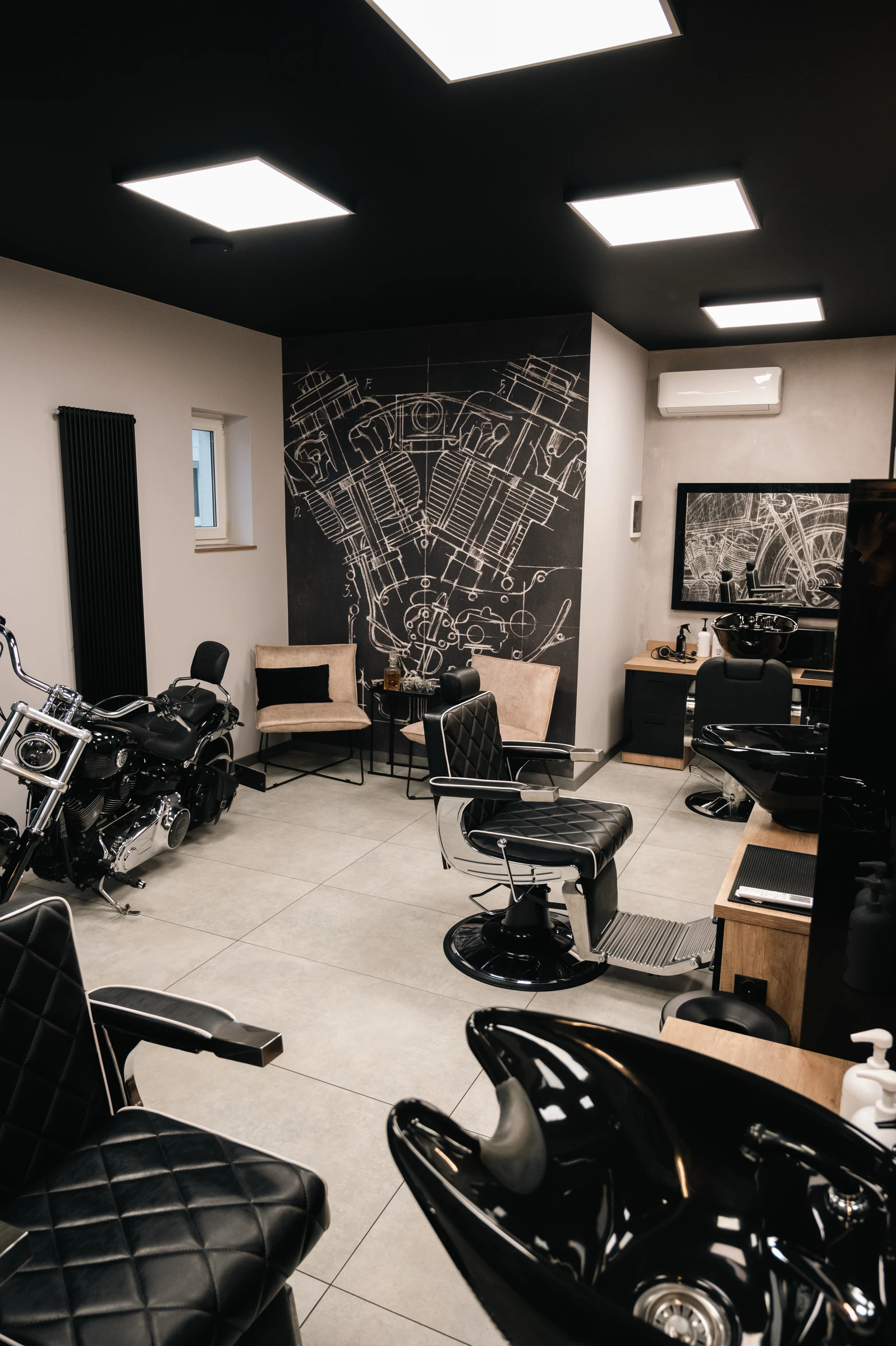 Barber Room z czarnymi fotelami, motorem i rysunkiem silnika na ścianie
